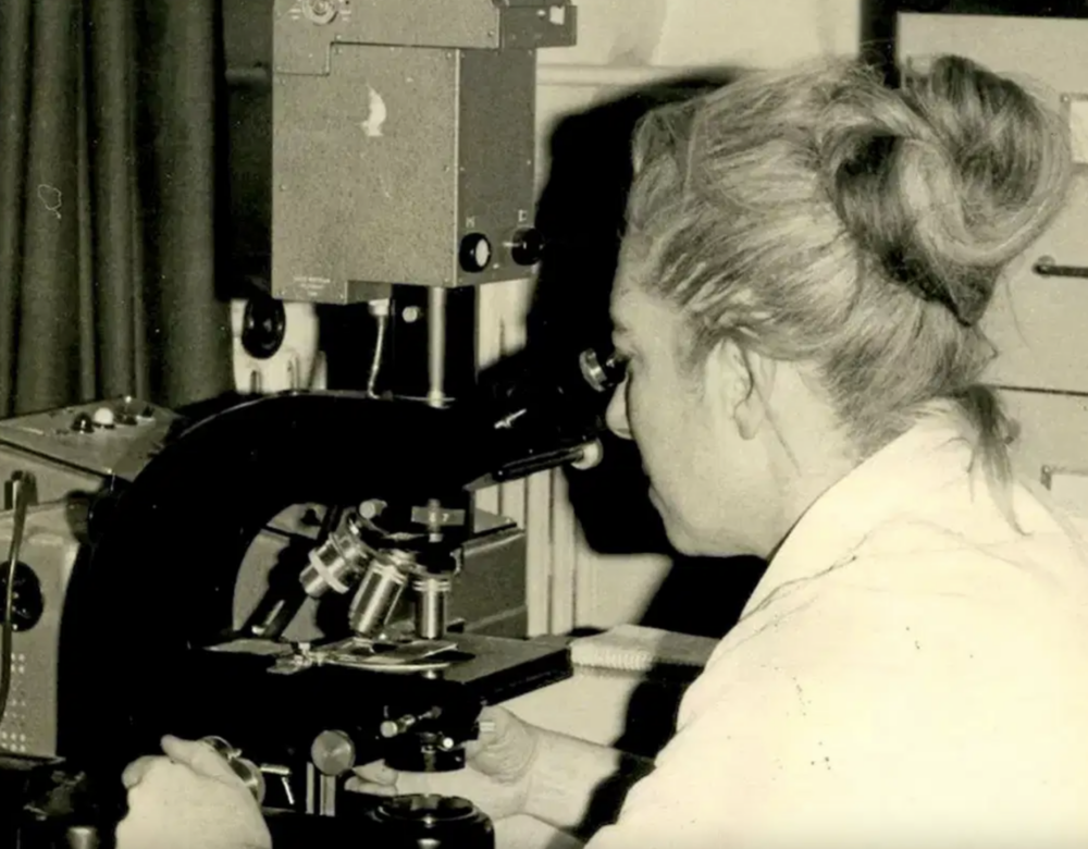 Black and white photo of woman looking into microscope